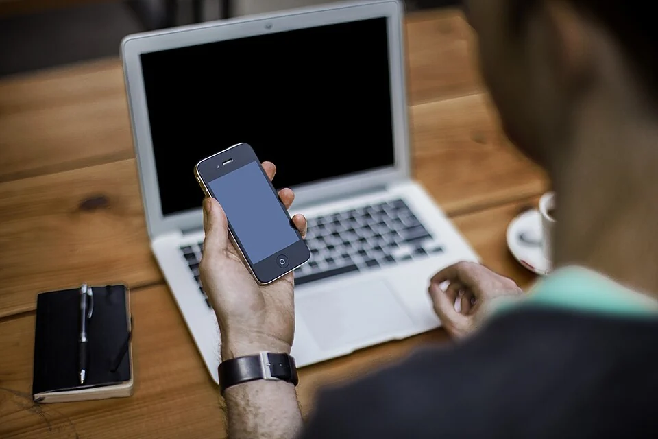 Zoeken met een smartphone en laptop aan een houten tafel